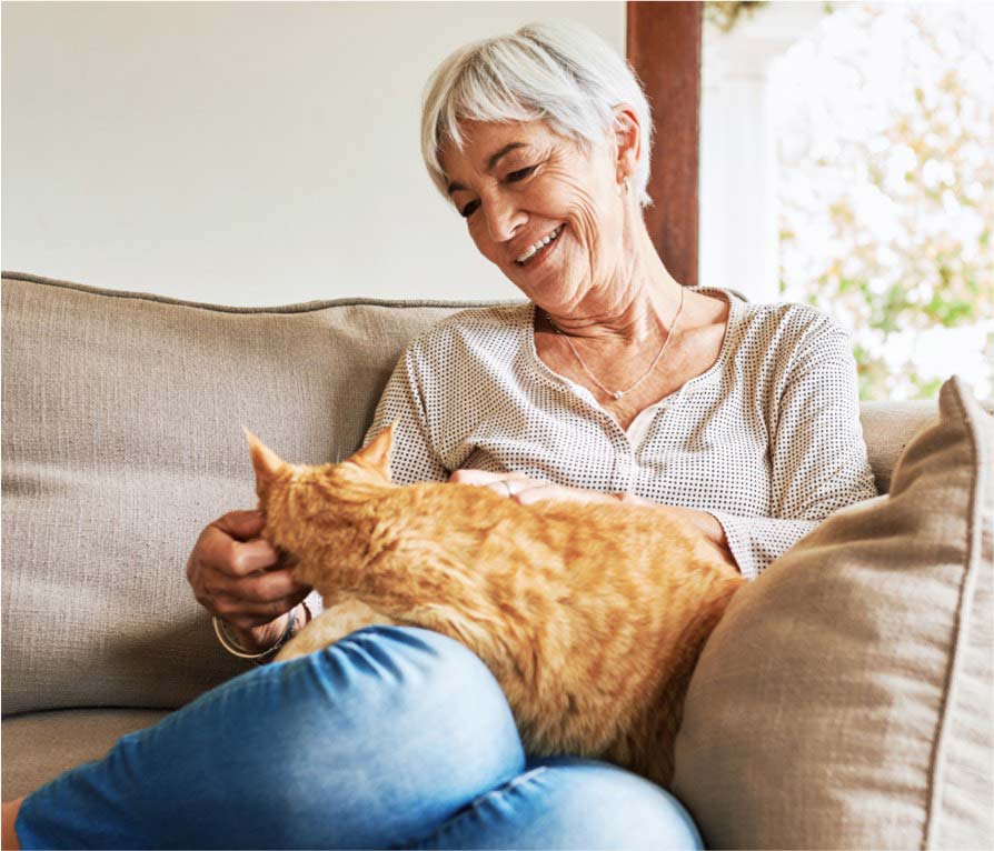 Elderly woman sitting on a couch while petting an orange cat on her lap