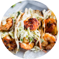 Three grilled shrimp tacos topped with shredded cabbage and sauce served in soft tortillas.