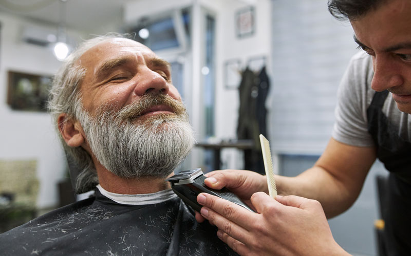 Man receiving a beard trim at a barbershop with a relaxed expression on his face.