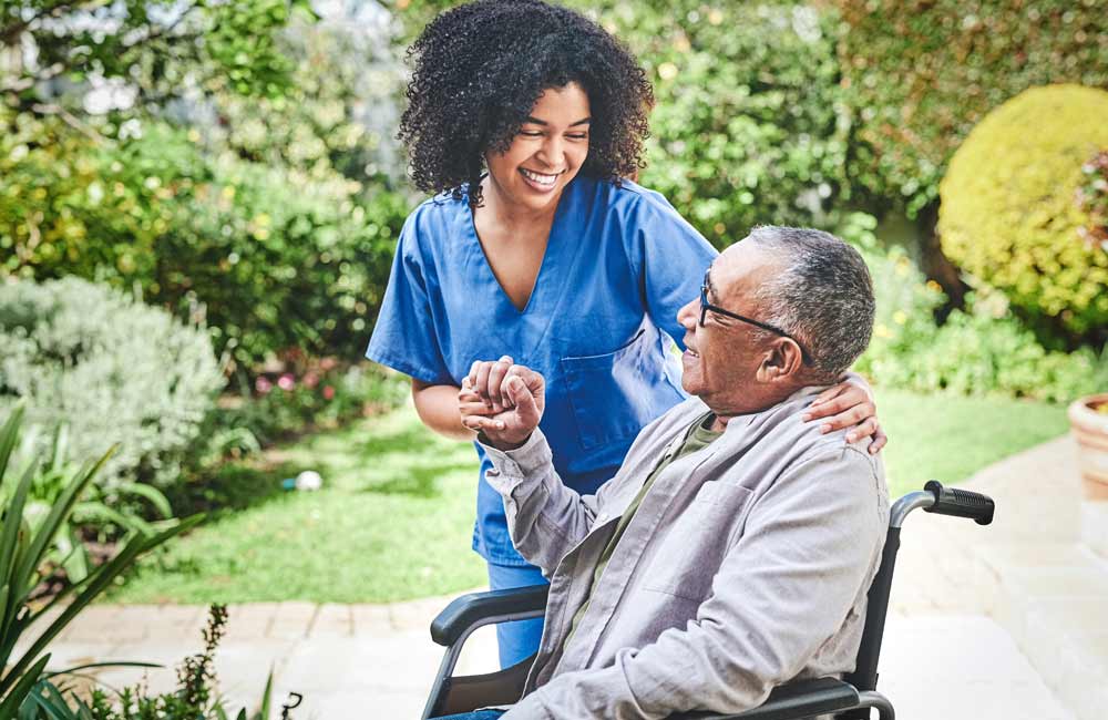 Caregiver smiling while interacting with senior man in wheelchair in a garden setting