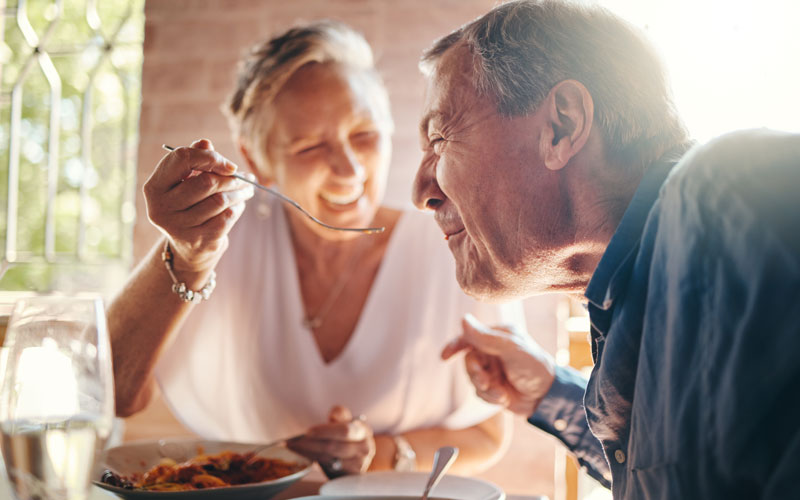 Elderly couple enjoying a meal together, with the woman feeding the man a spoonful of food.