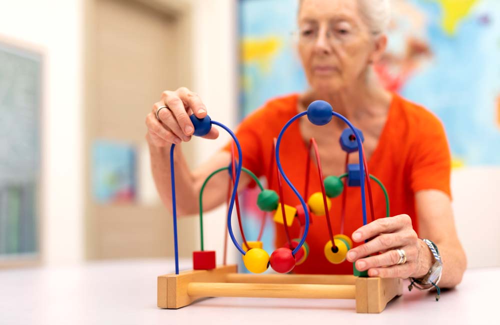 Elderly woman engaging with a bead maze toy during a memory care activity session.