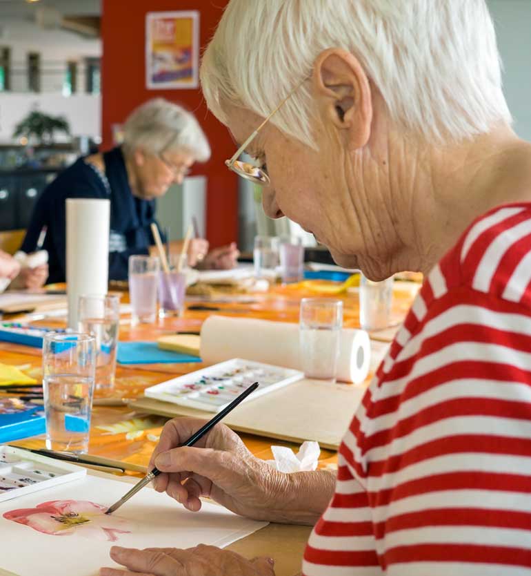 Elderly women engaged in watercolor painting at a table filled with art supplies
