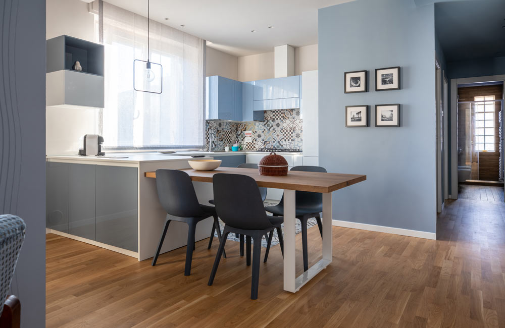Modern kitchen with wooden dining table and blue cabinets in a bright, airy apartment.