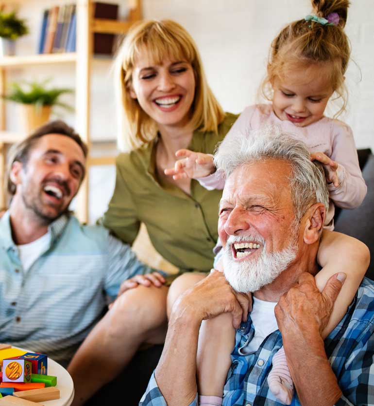 Senior man joyfully playing with his family, including a child on his shoulders and two adults laughing.