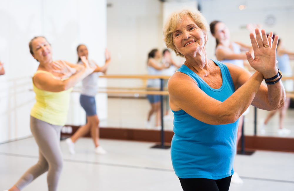 Group of senior women actively participating in a dance class, moving energetically and smiling.