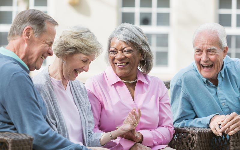 Four senior adults laughing and enjoying conversation while seated outdoors, showcasing active aging.